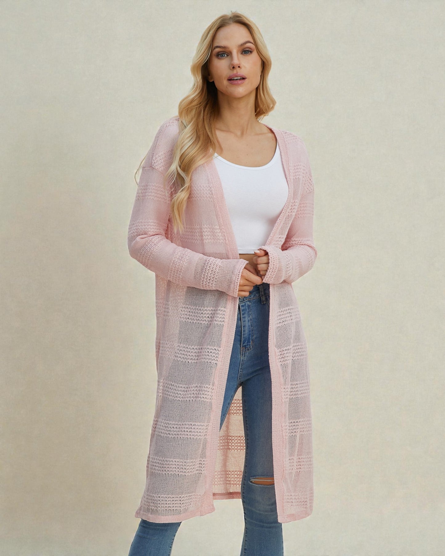 Woman wearing a long pink cardigan over a white top and blue jeans on a beige background