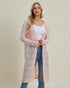Woman wearing a long pink cardigan over a white top and blue jeans on a beige background
