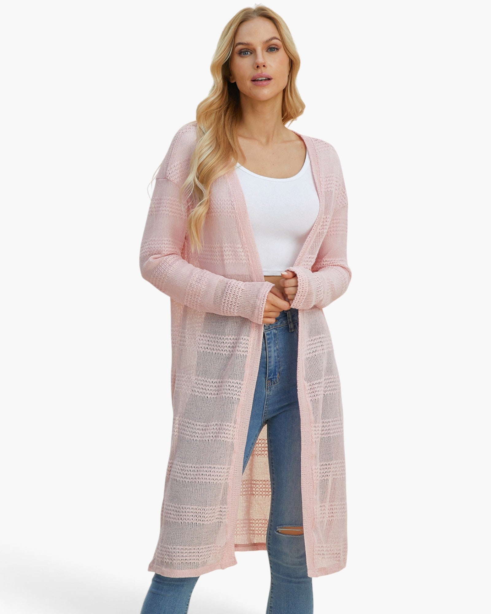A blonde woman modeling a long, light pink open-front cardigan with a textured knit pattern over a white tank top and blue jeans, set against a plain white studio background.
