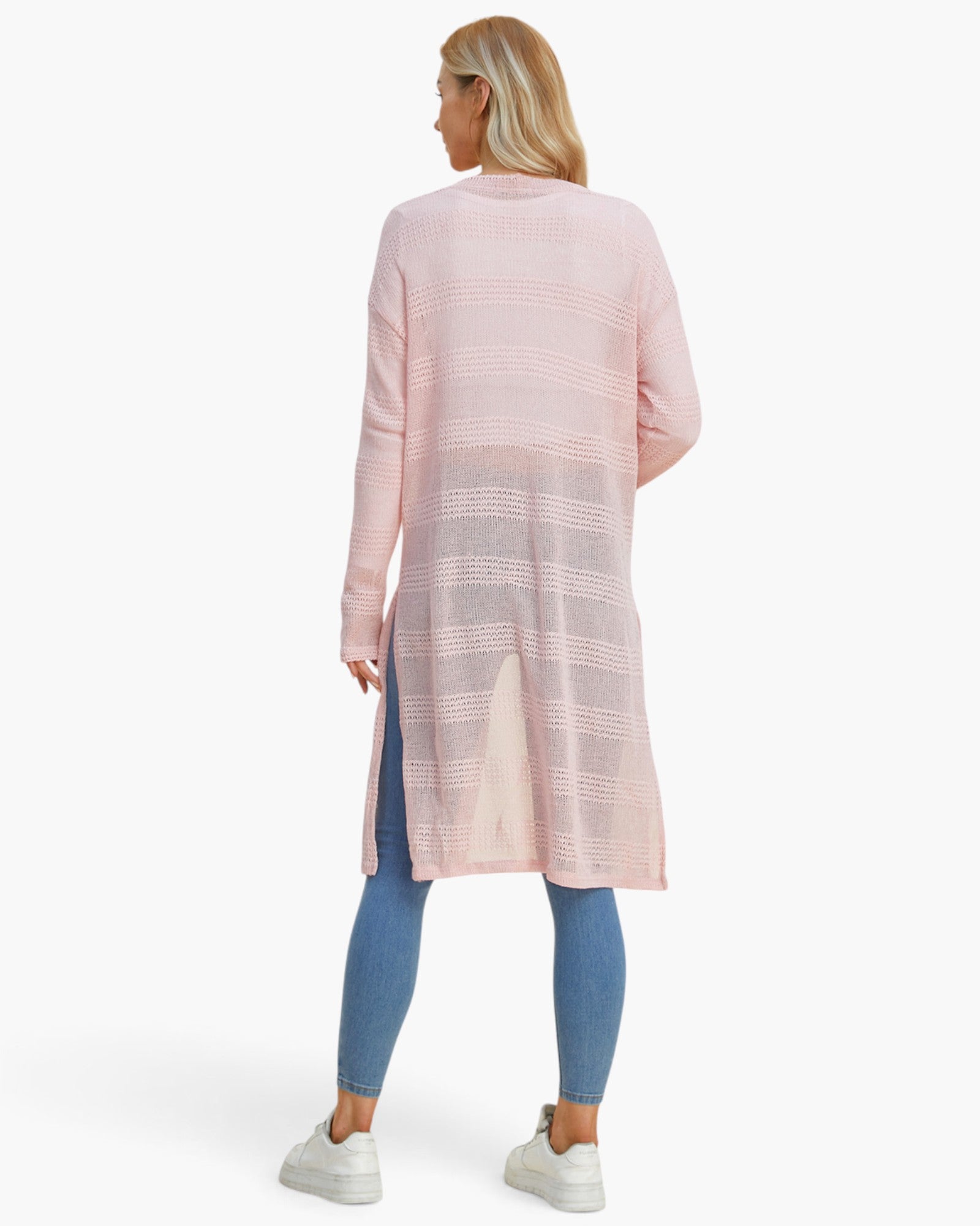 A woman shown from the back wearing a light pink open-front knit cardigan with horizontal textured stripes, paired with blue leggings and white sneakers, against a plain white studio background.