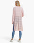 A woman shown from the back wearing a light pink open-front knit cardigan with horizontal textured stripes, paired with blue leggings and white sneakers, against a plain white studio background.