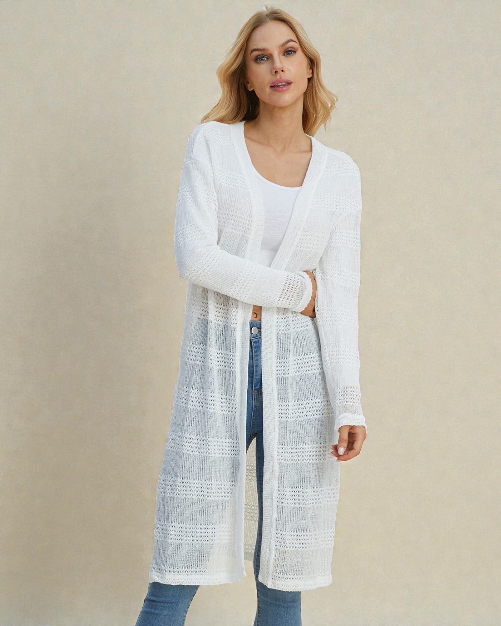 Woman wearing a long white cardigan over a white top and jeans on a beige background