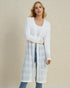 Woman wearing a long white cardigan over a white top and jeans on a beige background