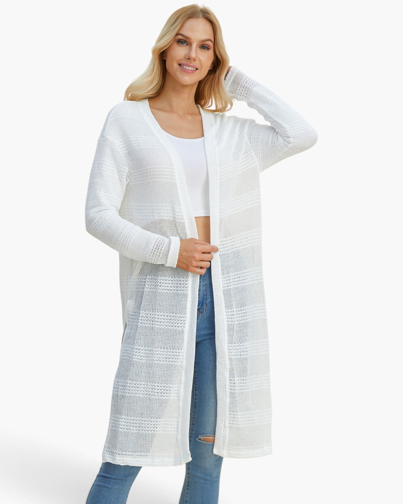 A woman modeling a long, open-front white knit cardigan with textured horizontal stripes over a white top and blue jeans, set against a plain white studio background.
