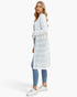 A woman modeling a white long-sleeve textured open-front cardigan or duster over a white top, paired with blue skinny jeans and white sneakers, against a plain white studio background.