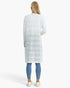 A woman viewed from behind wearing a white long-sleeve knit tunic with horizontal textured stripes, paired with blue leggings and white sneakers, against a plain white studio background.