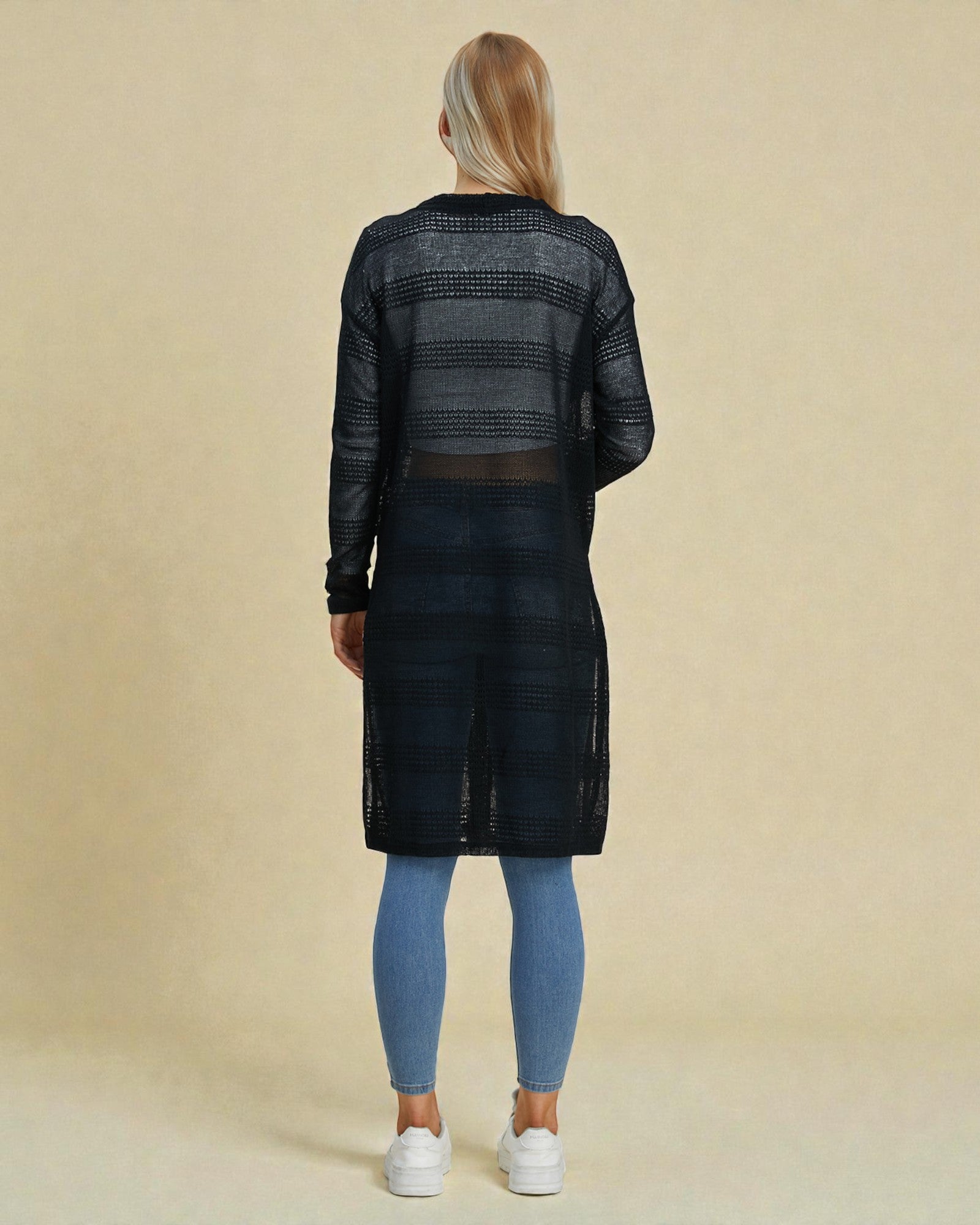 Person wearing a black textured dress with sheer panels on a beige background