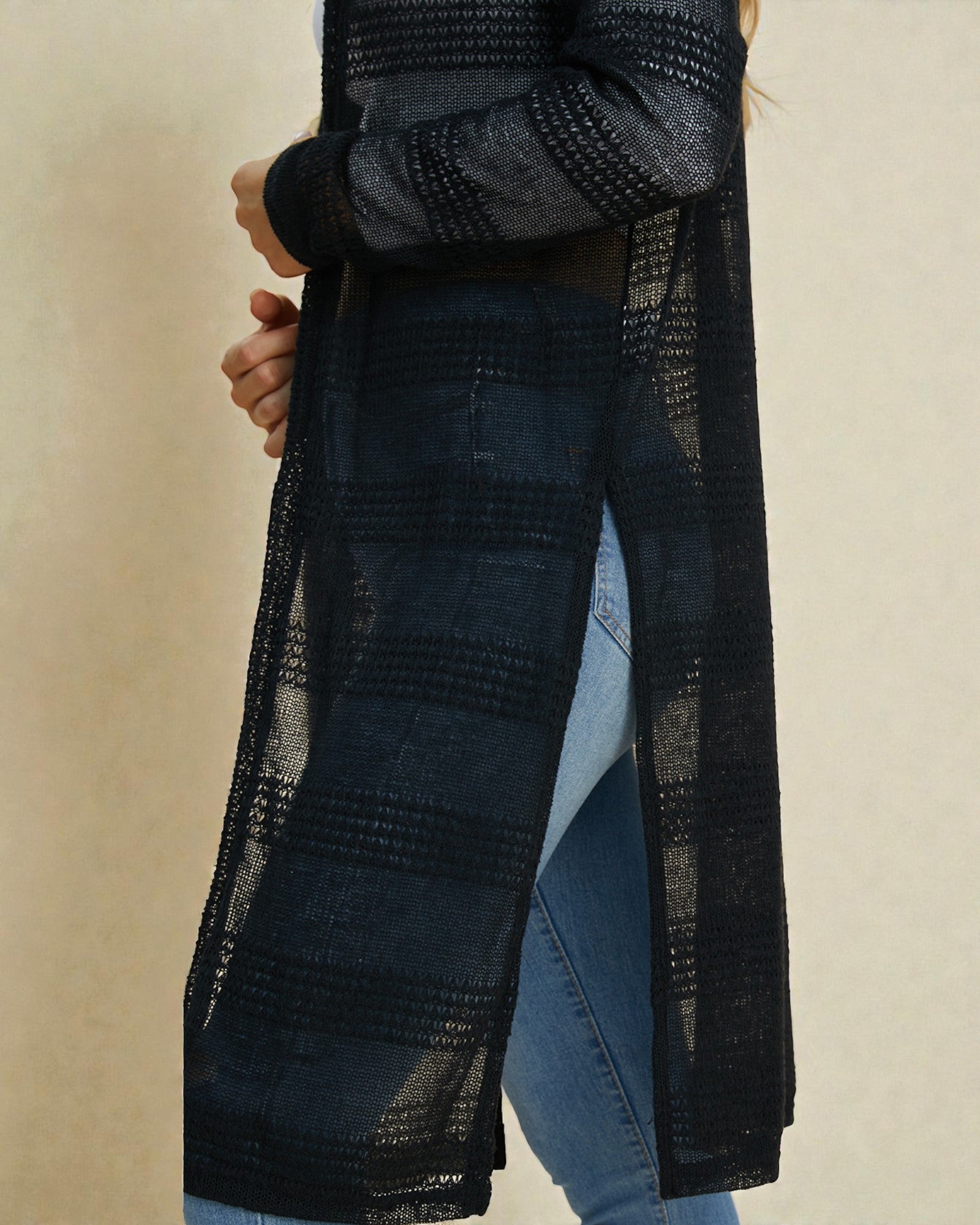 Person wearing a long black textured coat over a blue outfit on a beige background