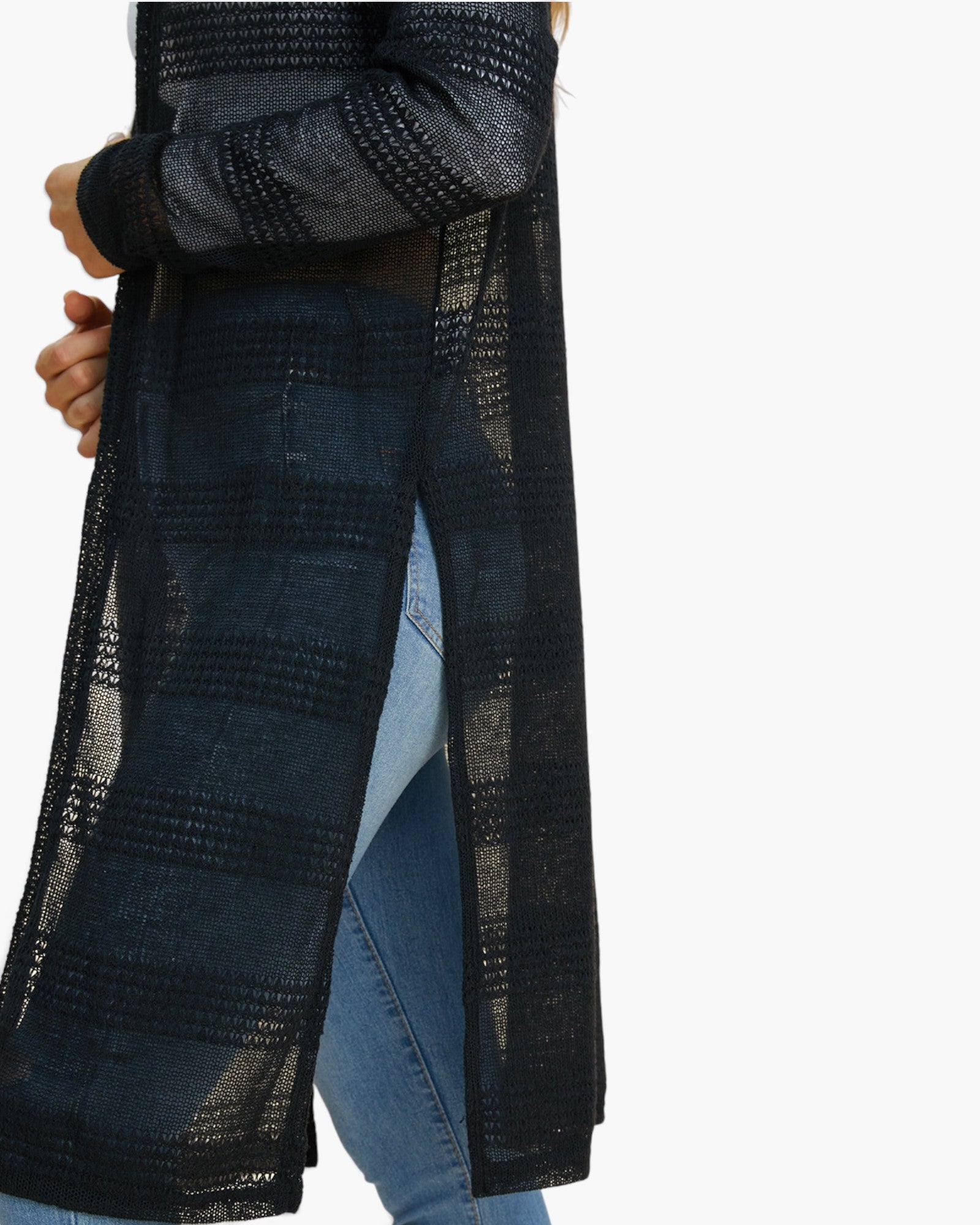 A close-up of a person wearing a long, open-front knit cardigan in a dark navy and black plaid pattern over blue jeans, shown against a plain white background.
