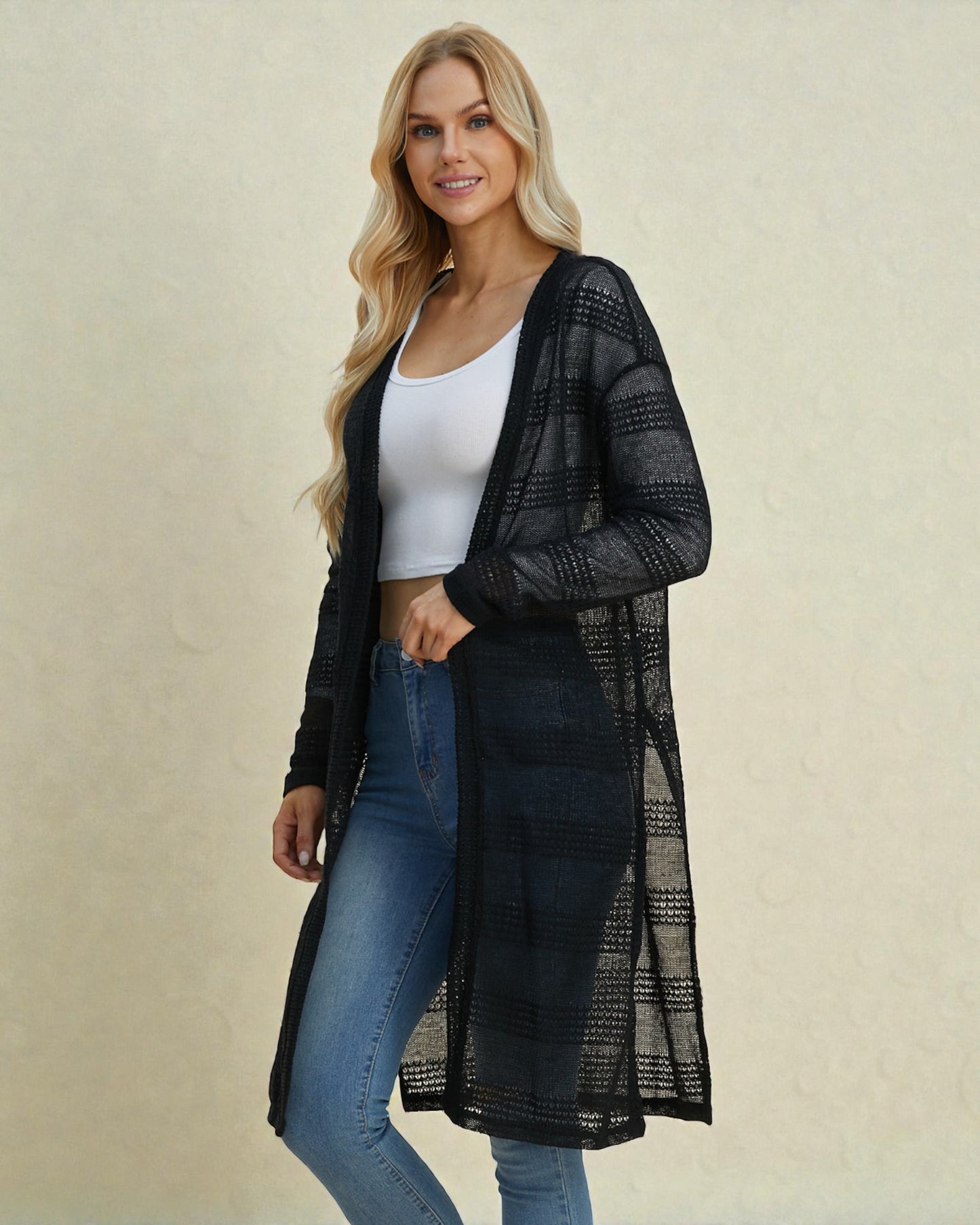 Woman wearing a black mesh cardigan over a white top and blue jeans on a beige background