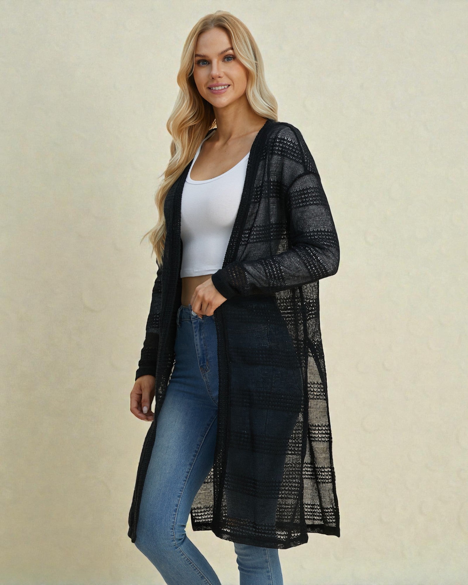 Woman wearing a black mesh cardigan over a white top and blue jeans on a beige background