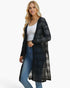 A woman modeling a long black open-front cardigan with a subtle plaid pattern over a white tank top and blue jeans, set against a plain white studio background.