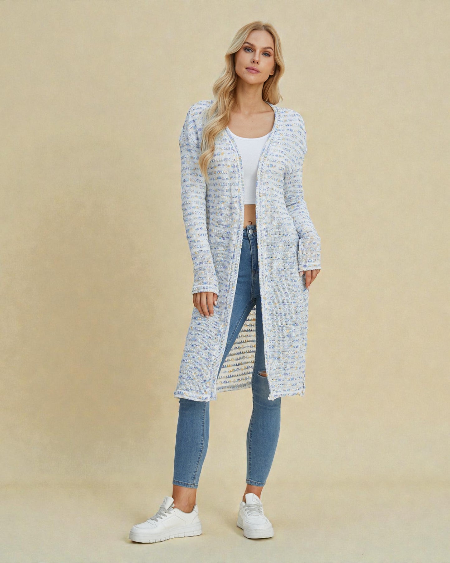 Woman wearing a long, light blue cardigan over a white top and jeans on a beige background