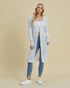 Woman wearing a long, light blue cardigan over a white top and jeans on a beige background