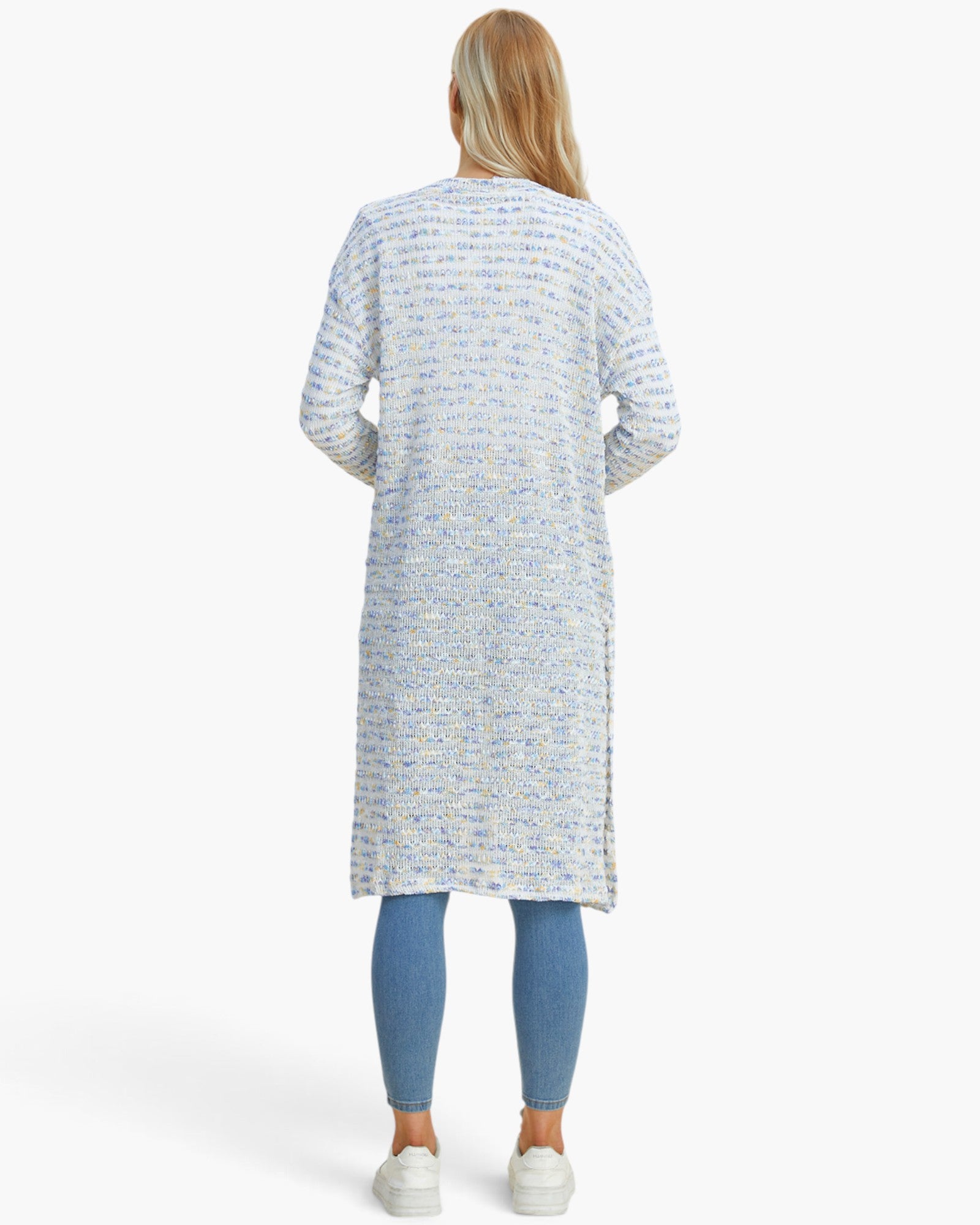 A woman viewed from the back wearing a long-sleeve, knee-length textured knit cardigan in a light blue and white pattern, paired with blue leggings and white sneakers, against a plain white studio background.