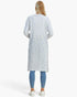 A woman viewed from the back wearing a long-sleeve, knee-length textured knit cardigan in a light blue and white pattern, paired with blue leggings and white sneakers, against a plain white studio background.