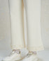 White textured pants with pearl details and white sneakers on a light gray background