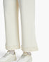 Close-up of a person wearing textured off-white wide-leg trousers with pearl trim at the hem, paired with white sneakers and white socks, against a plain light background.