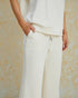 Person wearing a white outfit with wide-leg pants against a textured beige background