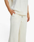 A close-up of a model wearing textured off-white knit pants with a drawstring waist and a matching top, shown against a clean white background.