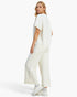 A woman modeling a matching off-white lounge set consisting of a short-sleeve top with lace trim and wide-leg cropped pants, paired with white sneakers against a plain white studio background.