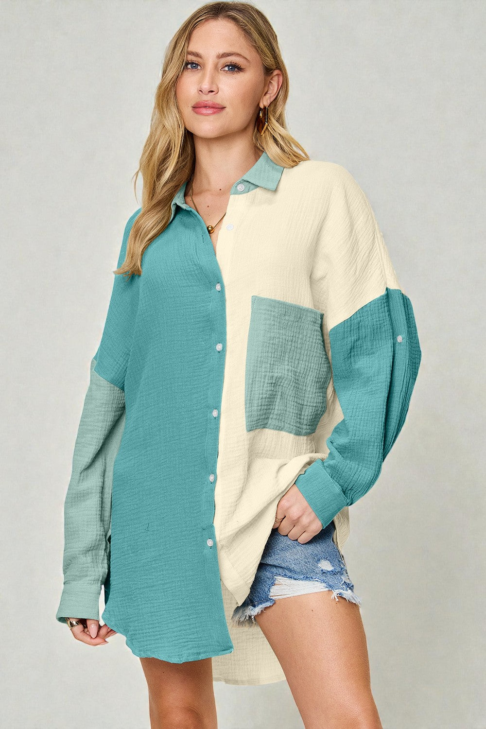 Woman wearing a cream and teal color-blocked shirt with denim shorts on a plain background