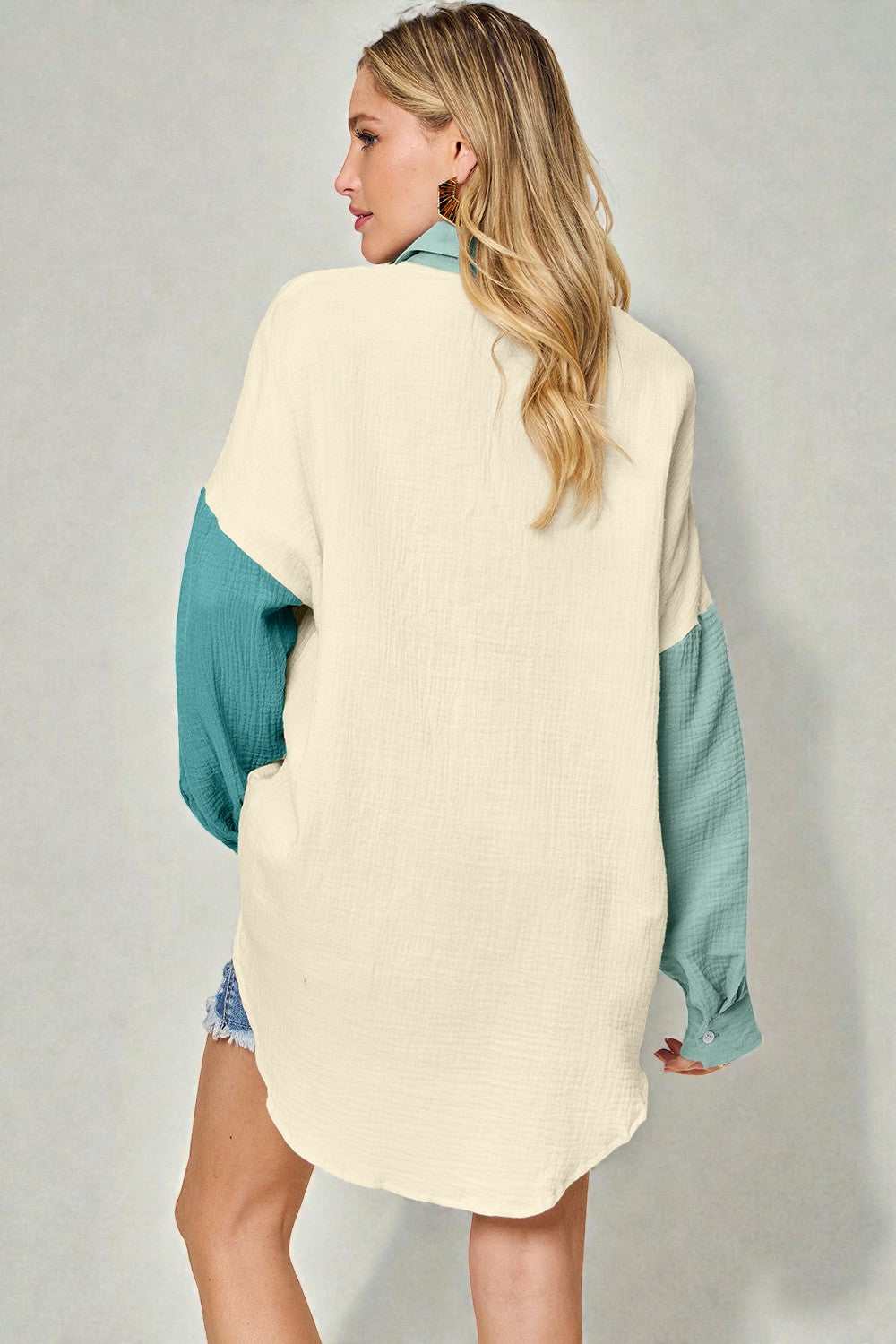 Woman wearing a cream and teal color-blocked sweater against a gray background