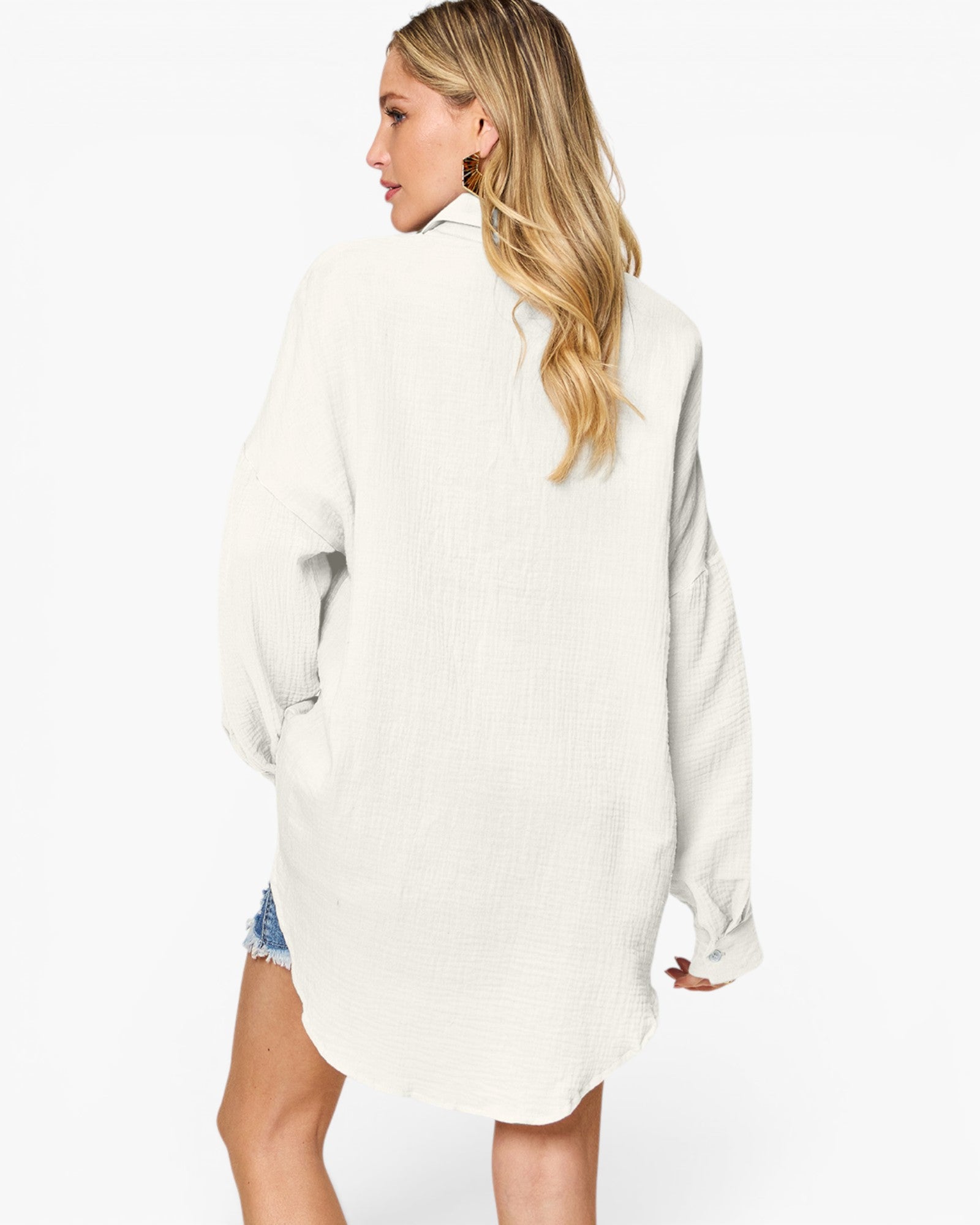 A woman shown from the back wearing an oversized off-white textured shirt dress, paired with denim shorts, against a plain white studio background.