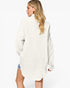 A woman shown from the back wearing an oversized off-white textured shirt dress, paired with denim shorts, against a plain white studio background.