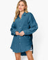 A woman modeling a blue textured button-up shirt dress with long sleeves and a high-low hem against a plain white background.