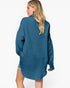 A woman shown from the back wearing an oversized textured blue button-up shirt, photographed against a clean white studio background.