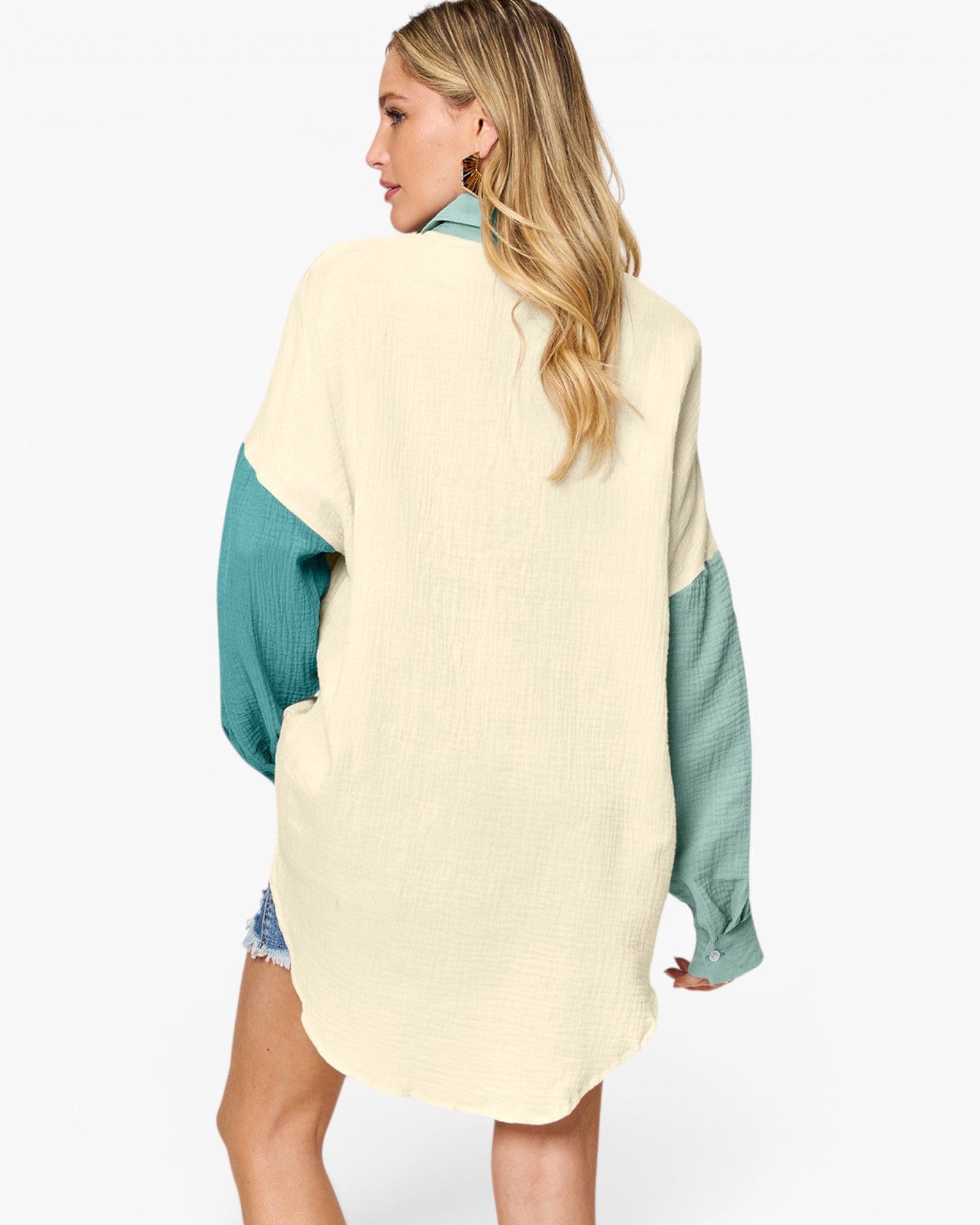 A woman shown from the back wearing a loose, oversized long-sleeve top with a cream body and teal sleeves, photographed against a plain light gray studio background.