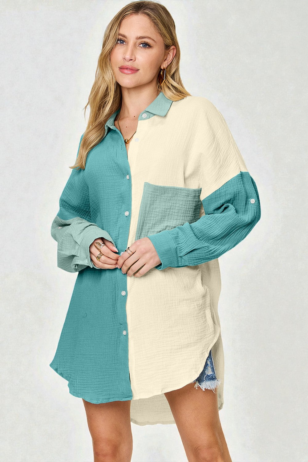 Woman wearing a color-blocked shirt with teal and beige sections on a plain background