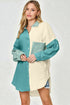 Woman wearing a color-blocked shirt with teal and beige sections on a plain background