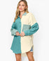 A woman modeling a color-block button-up shirt dress with one side in teal and the other side in cream, paired with denim shorts against a plain white background.
