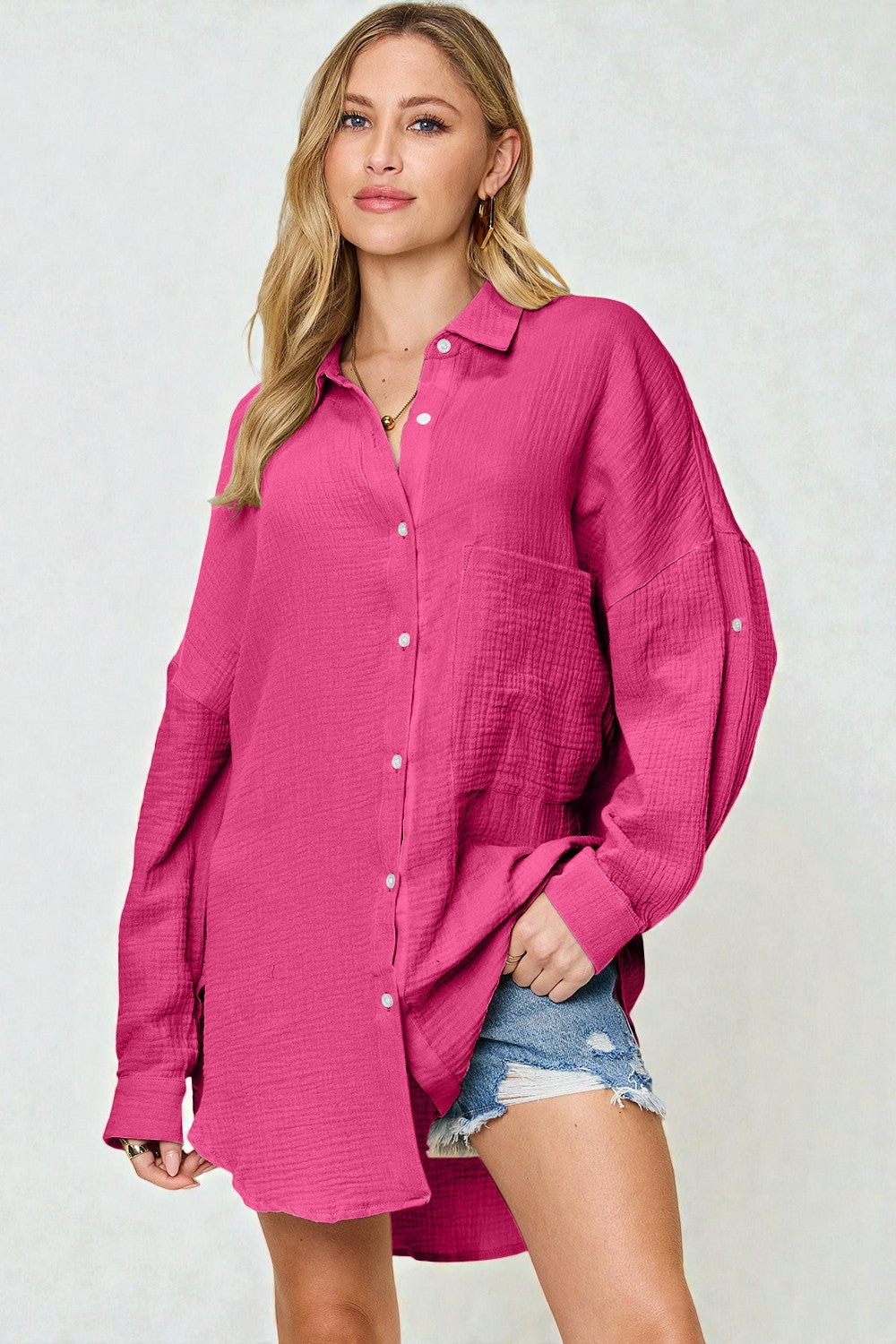 Woman wearing a bright pink shirt over denim shorts on a white background