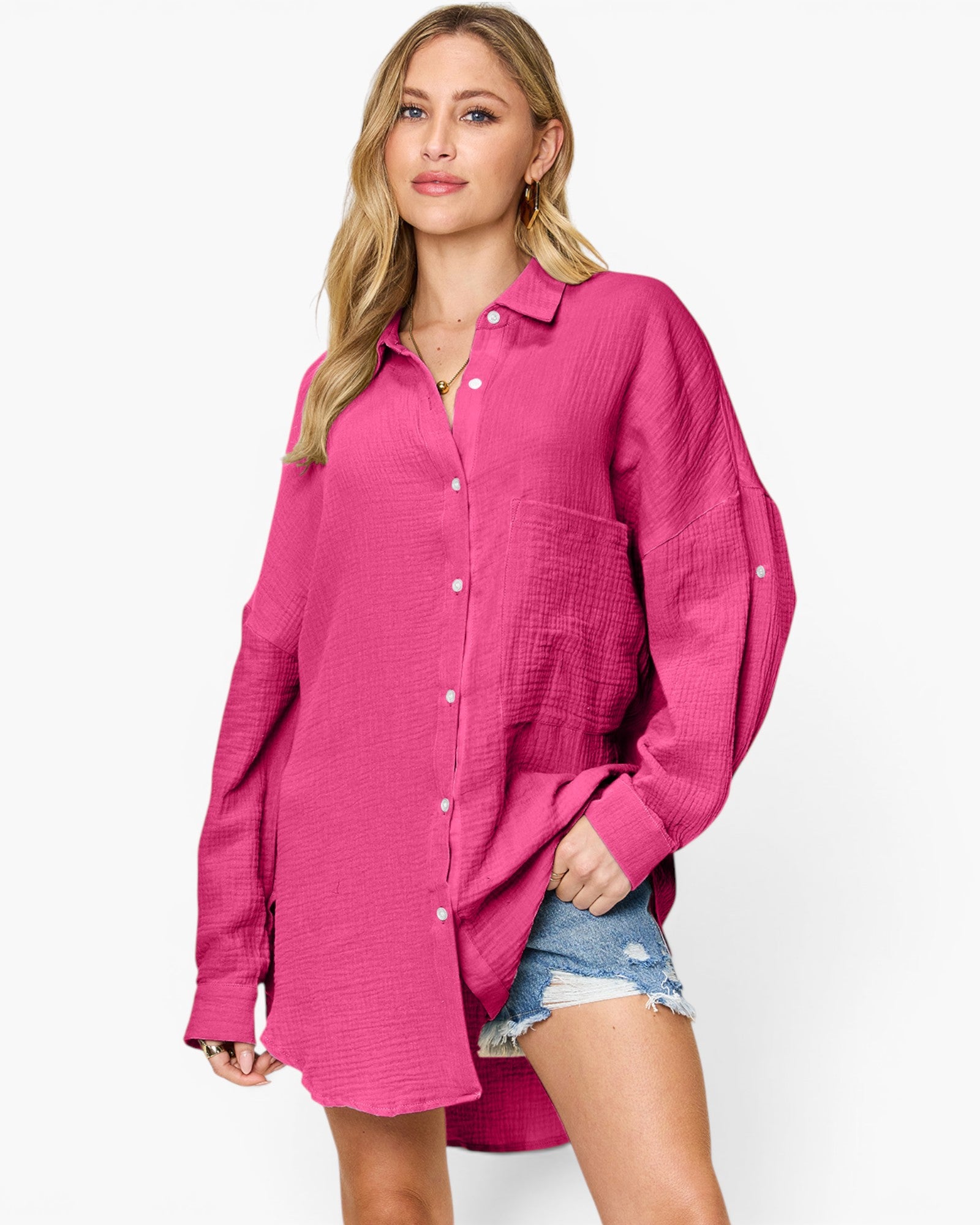 A woman modeling a bright pink textured button-up shirt with a collar and front pockets, paired with denim shorts, against a plain white studio background.