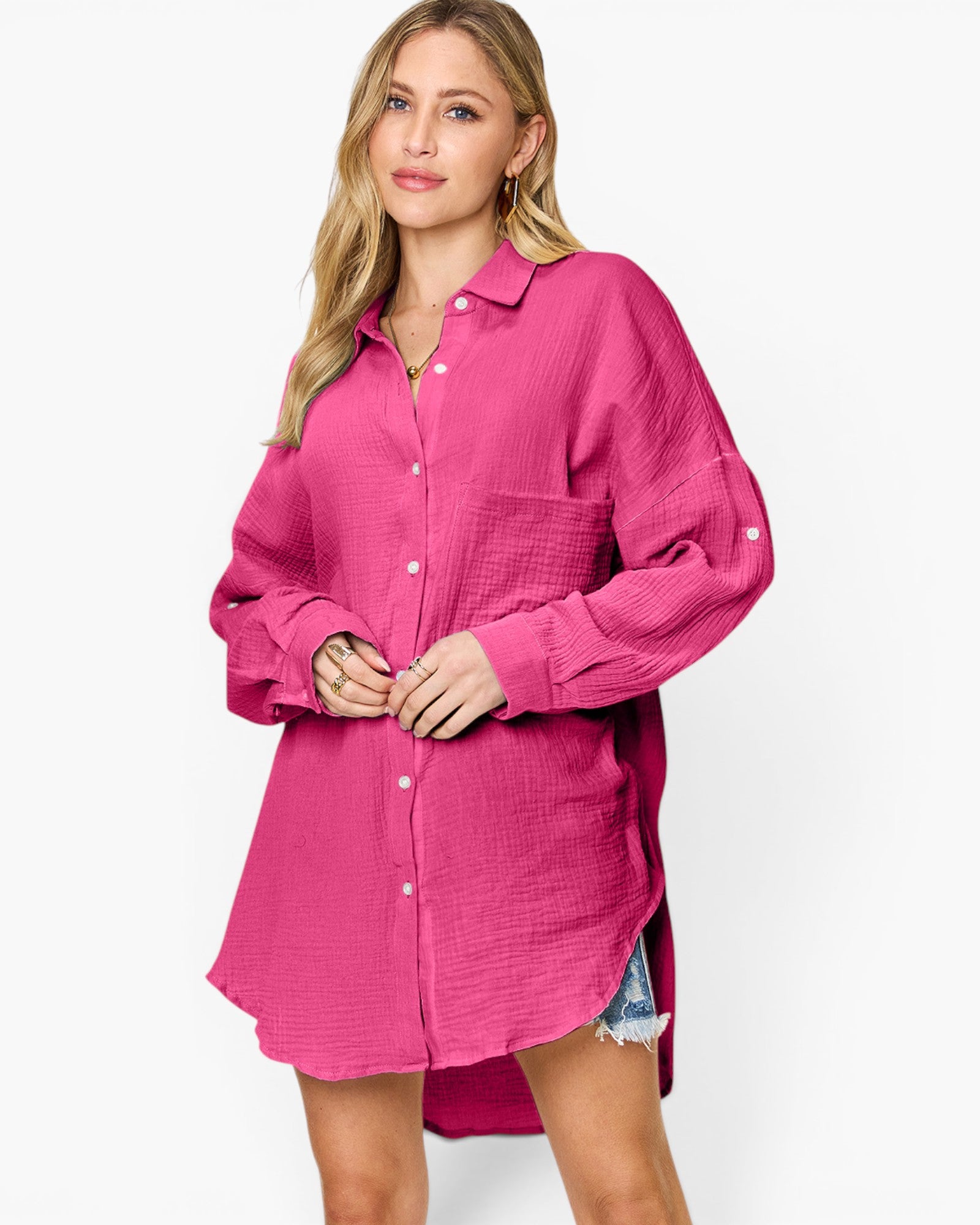 A woman modeling a bright pink textured button-up shirt dress with long sleeves and a relaxed fit, photographed against a clean white studio background.
