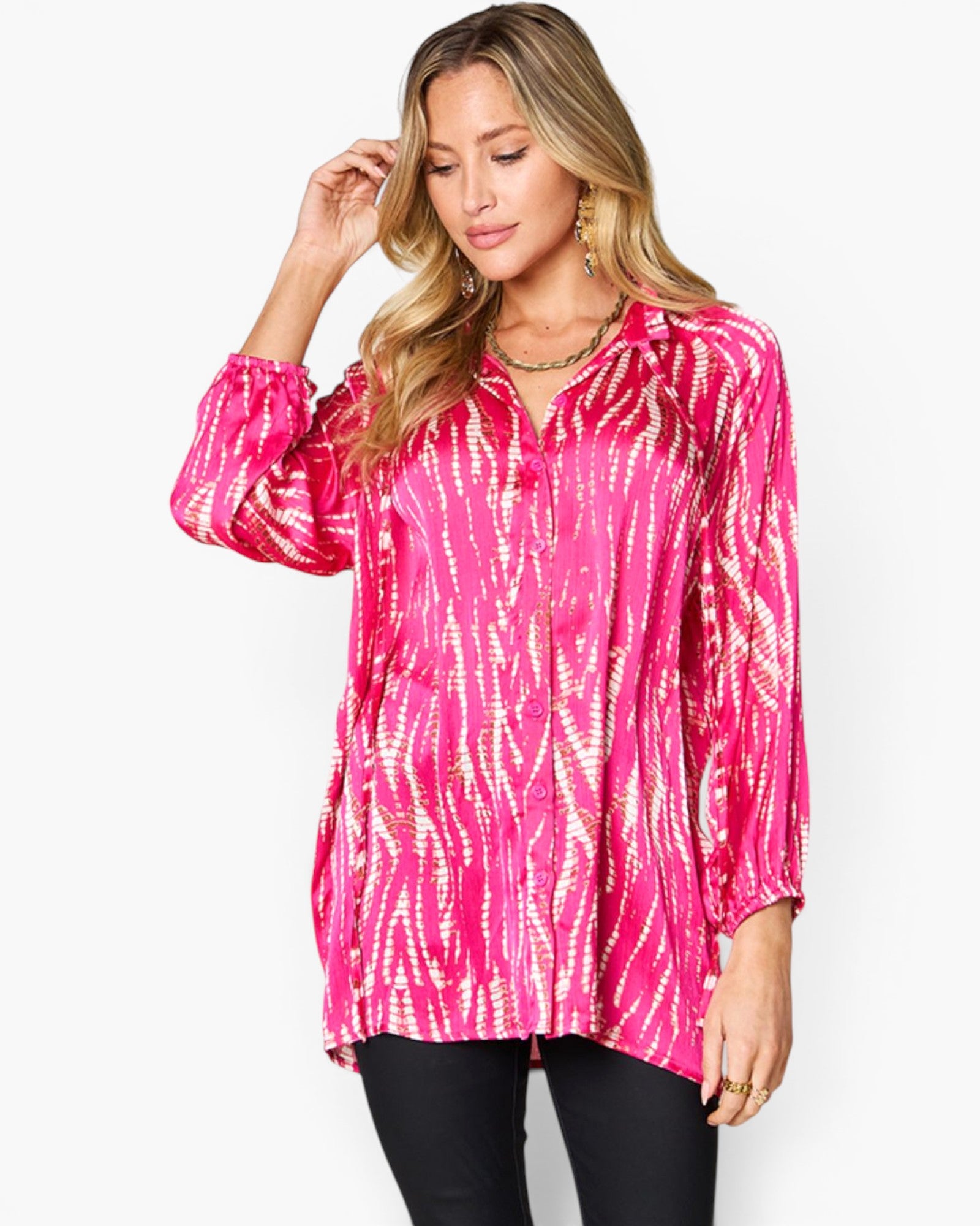 A woman modeling a bright pink long-sleeve button-up shirt with a white tie-dye pattern, paired with black pants, against a plain white background.