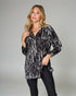Woman wearing a black and white patterned long-sleeve top against a gray background