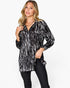 A woman modeling a black and white abstract patterned long-sleeve button-up shirt with black pants, set against a plain white studio background.