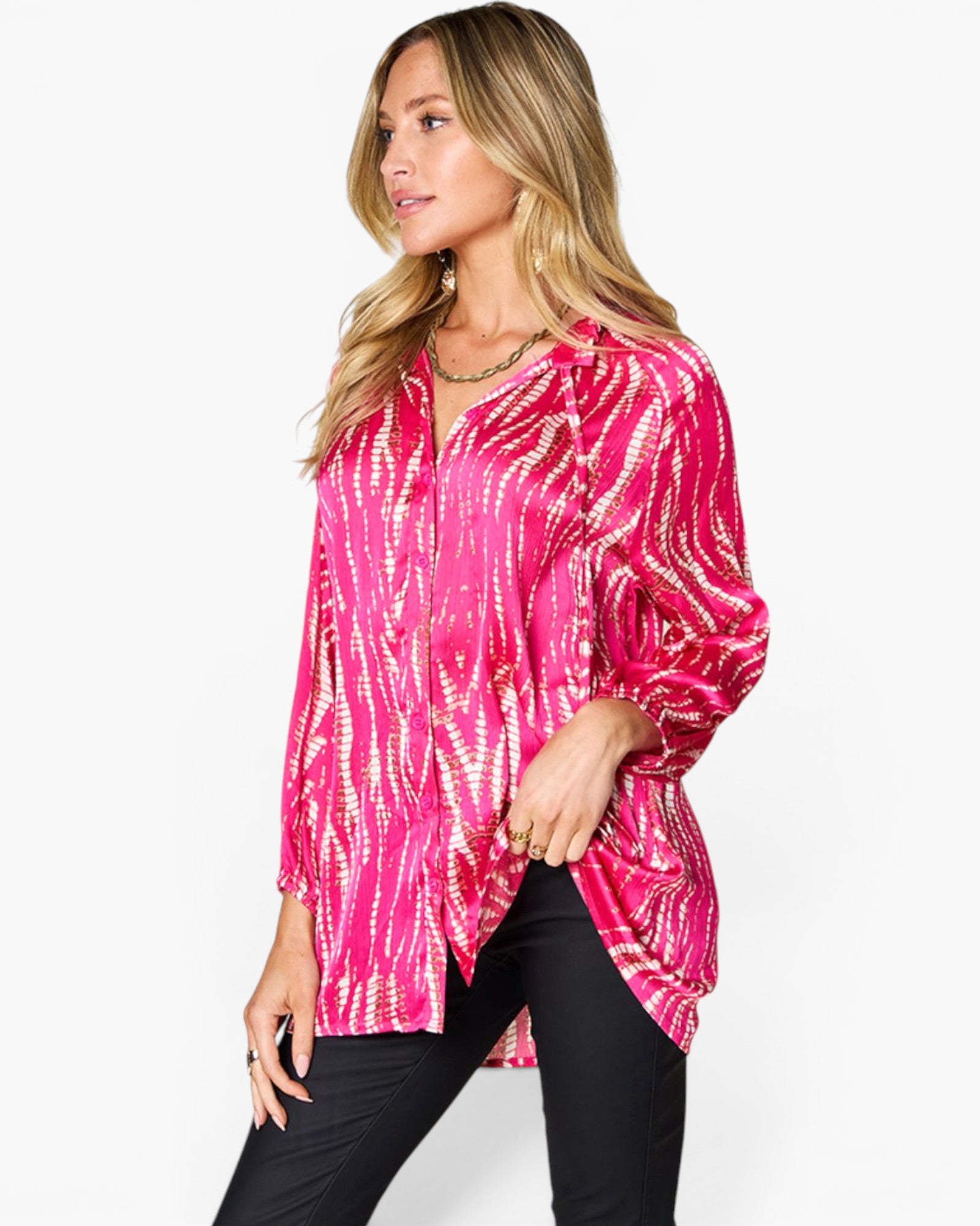 A woman wearing a vibrant pink long-sleeve blouse with a gold tie-dye pattern, paired with black pants, photographed against a clean white background.