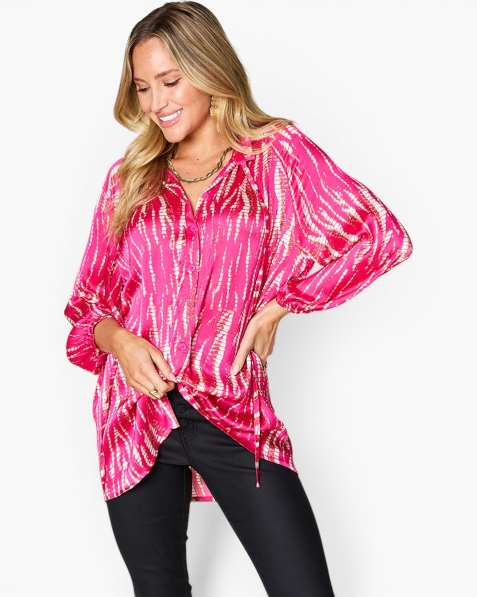 A woman wearing a bright pink and white tie-dye patterned blouse with balloon sleeves, paired with black pants, against a plain white studio background.