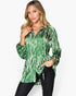 A woman modeling a green and white tie-dye patterned long-sleeve blouse with black pants, set against a plain light gray background.