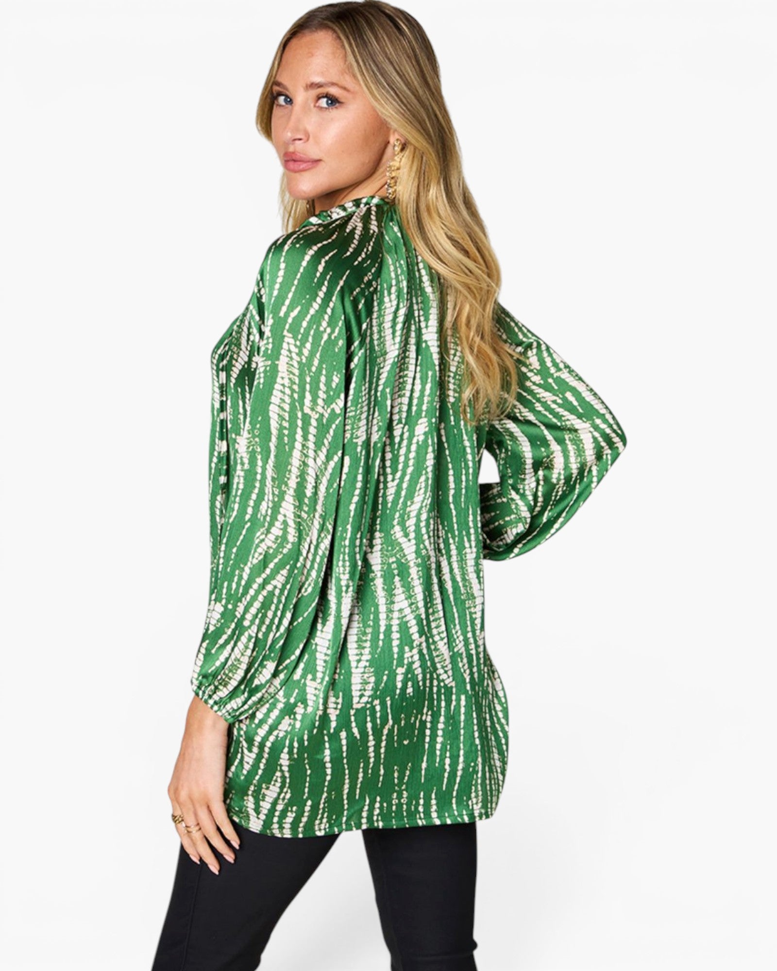 A woman modeling a green and white abstract patterned long-sleeve top, shown from a three-quarters back view against a plain white background.