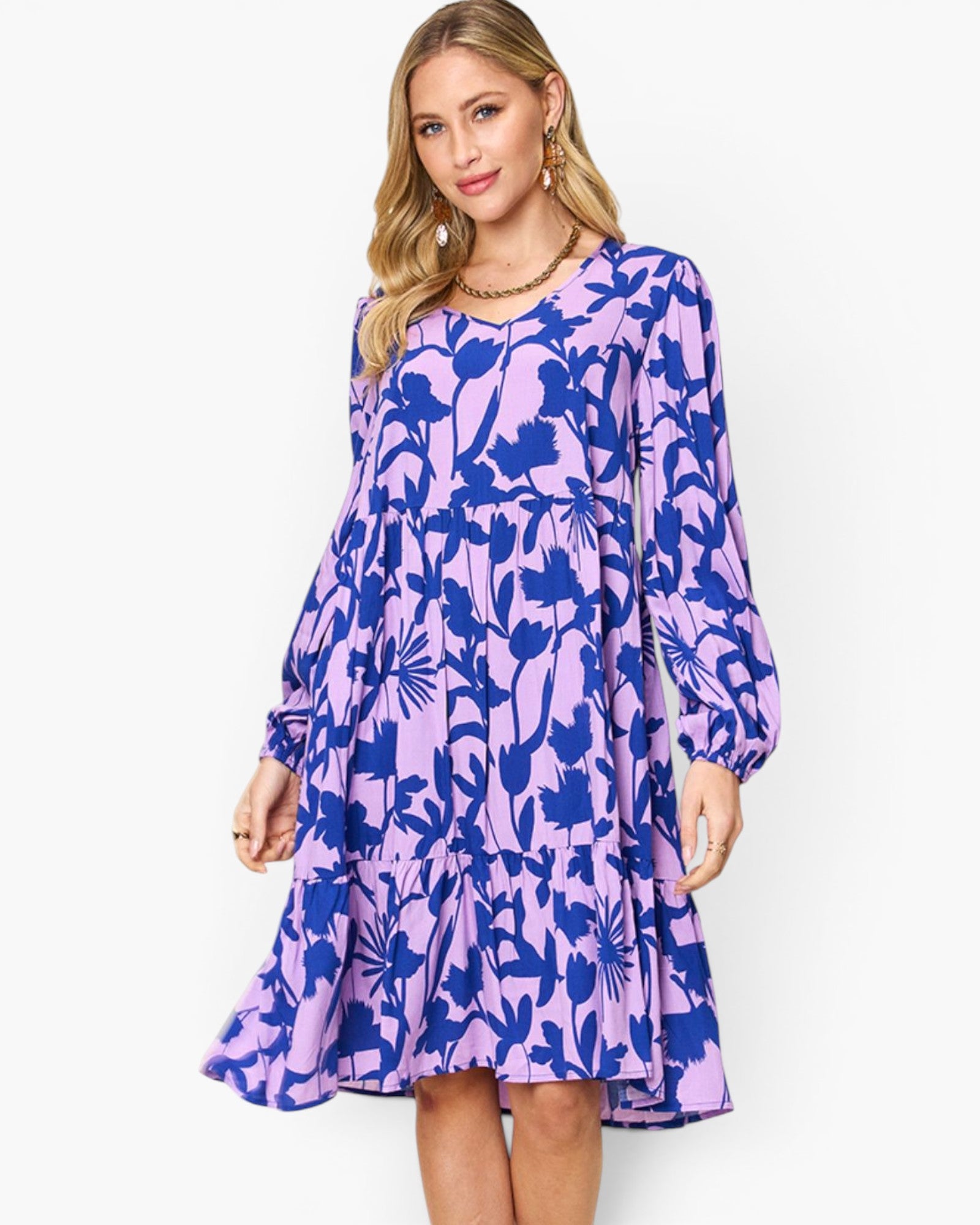 A woman modeling a long-sleeve tiered dress with a purple and blue floral pattern against a plain white background.