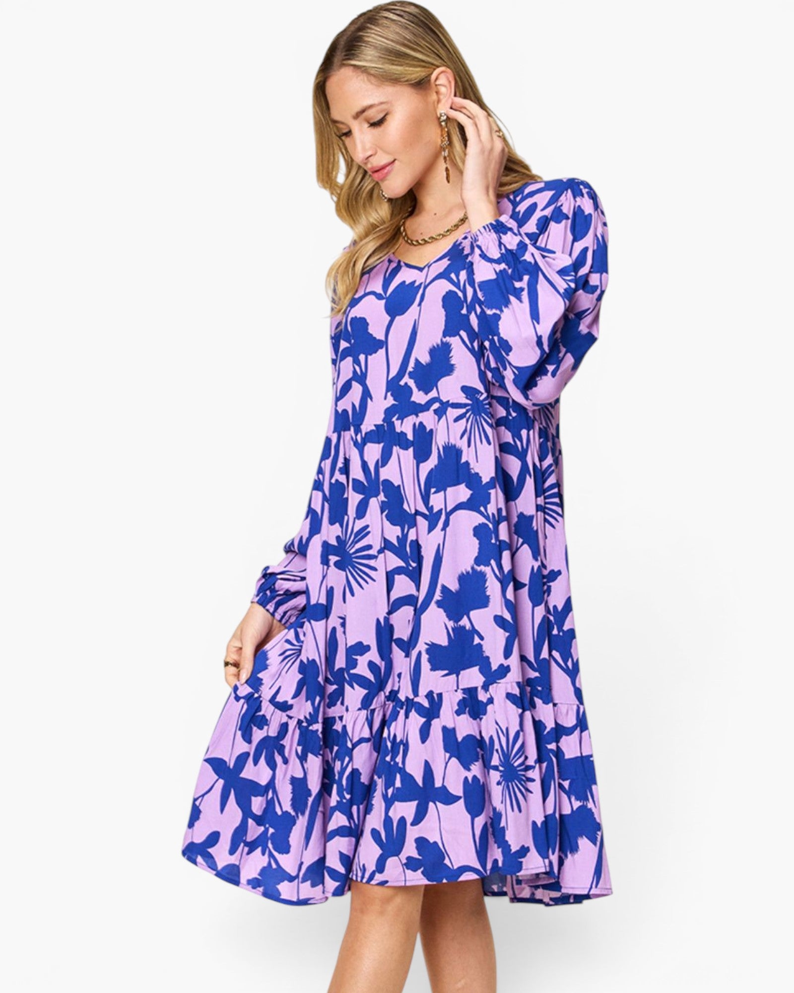 A woman modeling a long-sleeve midi dress with a purple and blue floral pattern, set against a plain white studio background.