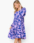 A woman modeling a long-sleeve midi dress with a purple and blue floral pattern, set against a plain white studio background.