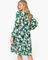 A woman modeling a long-sleeve midi dress with a green and cream abstract floral pattern, shown from a three-quarter back angle against a plain white background.