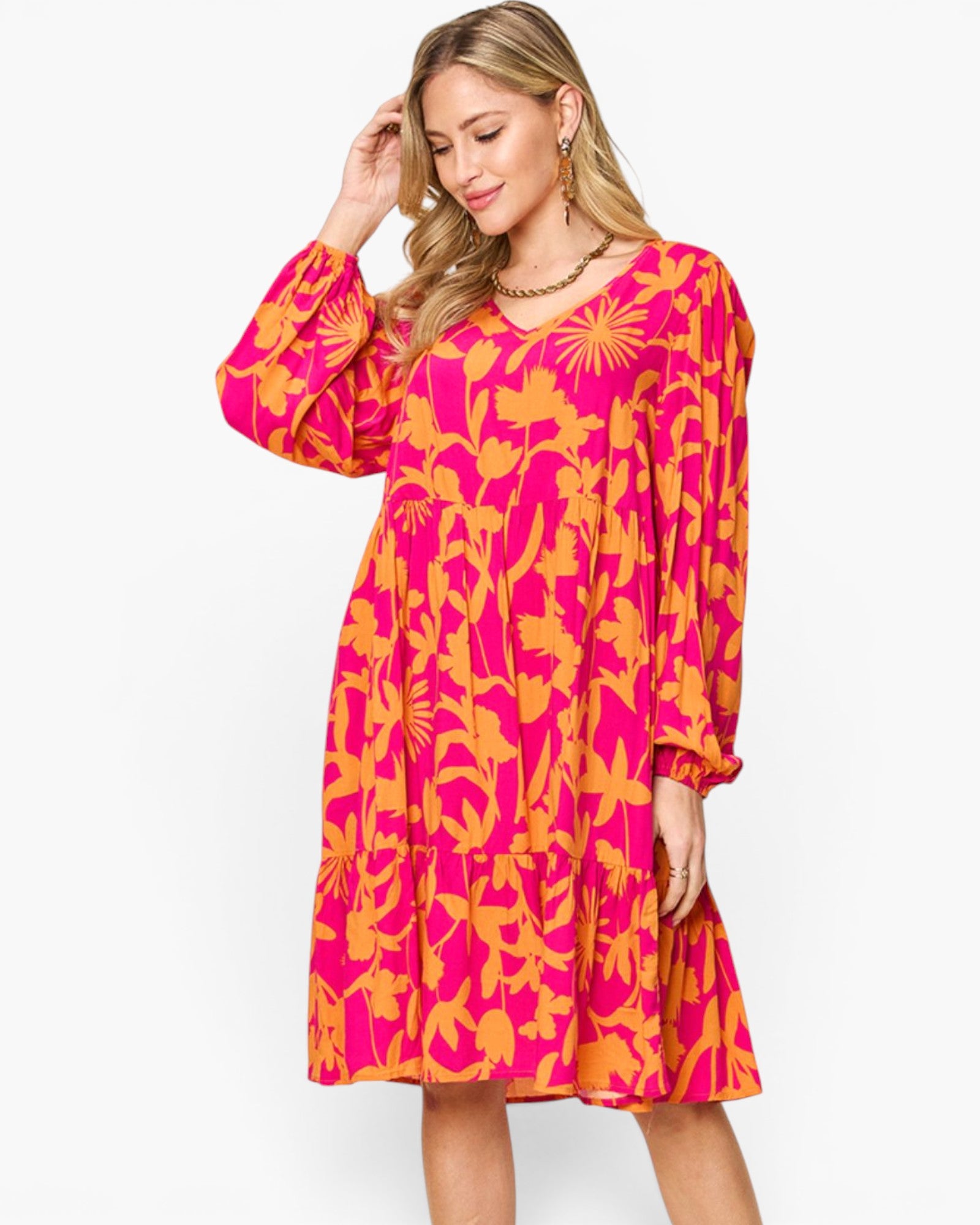 A woman modeling a long-sleeve V-neck midi dress with a vibrant pink and orange floral pattern, set against a plain white studio background.